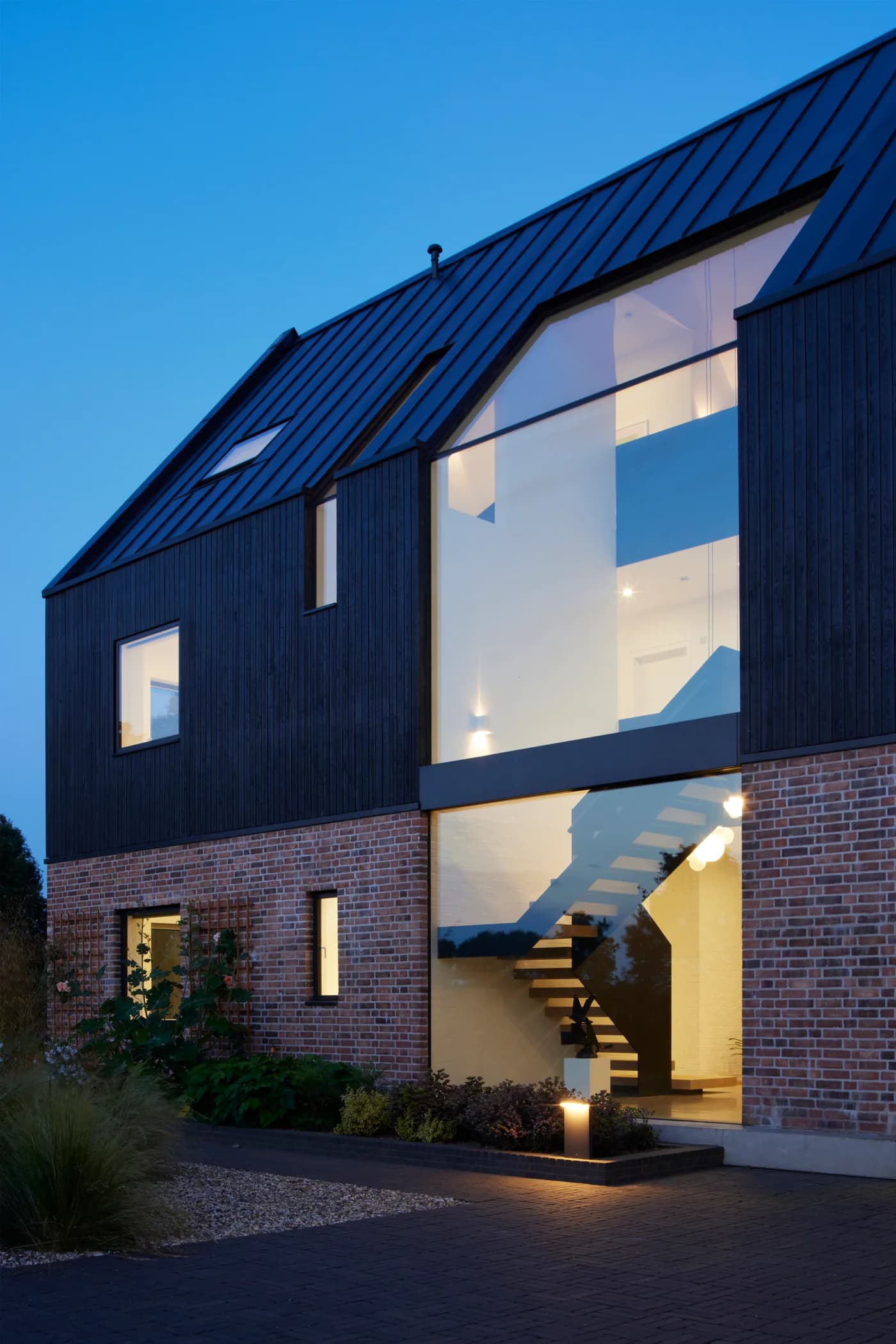 Glazed stairwell and roof openings in a dark-clad house at dusk