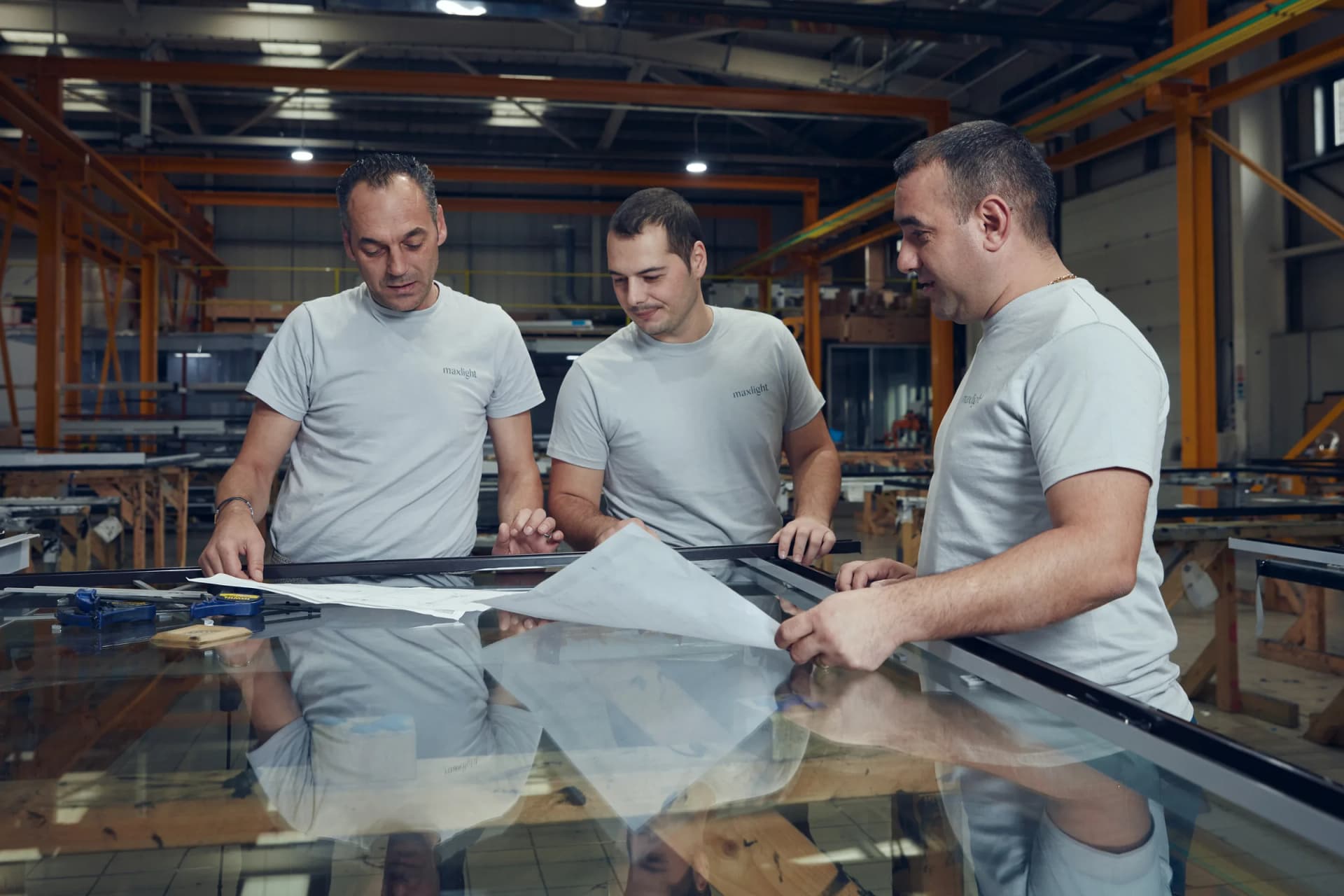 Three Maxlight team members reviewing drawings beside a glazed frame in the factory