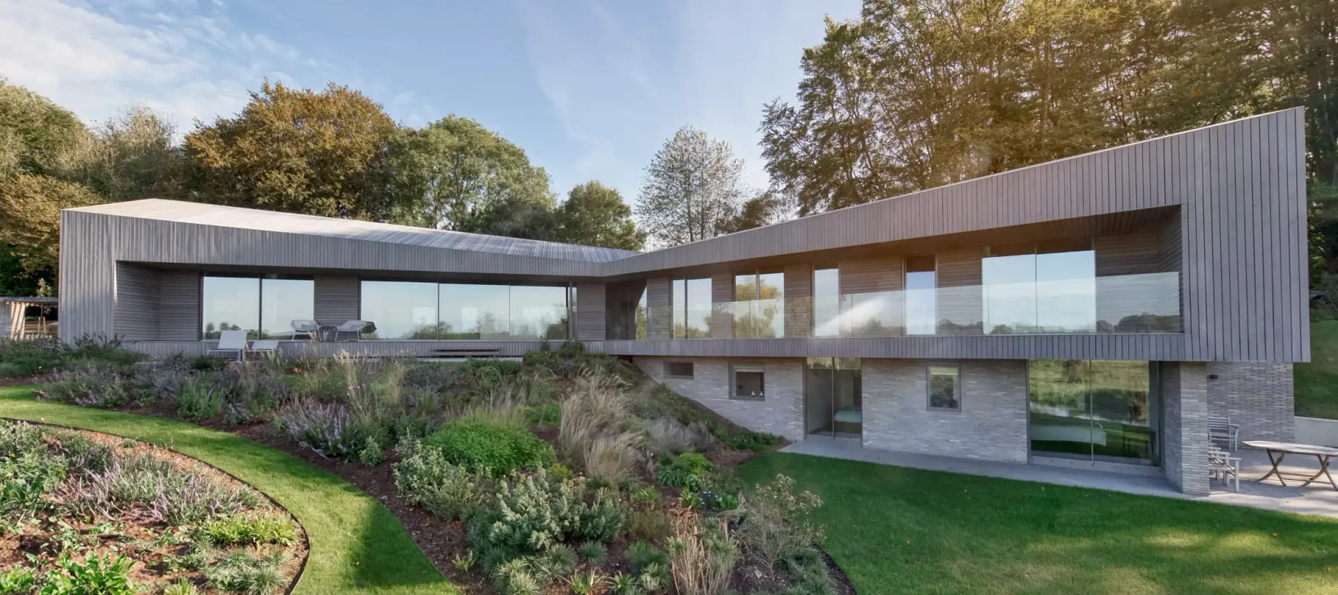 Slim-framed Maxlight glazing: a long uninterrupted glass elevation wrapping a contemporary timber-clad house above a brick base