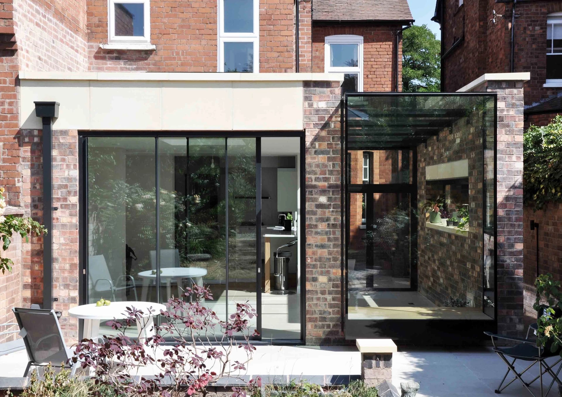 Rear brick extension with sliding glass doors and a projecting glazed bay opening onto a garden terrace.