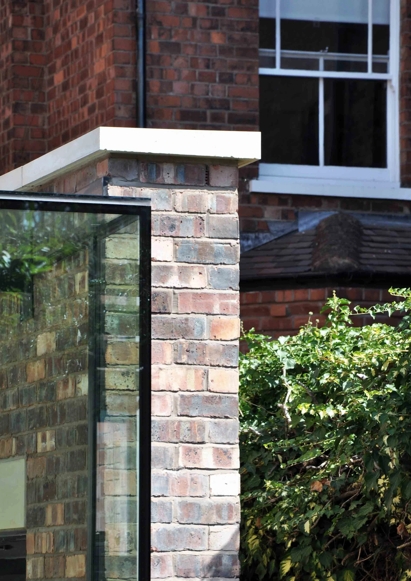 Glass edge beside a brick pier with a pale coping stone, with the original house behind.