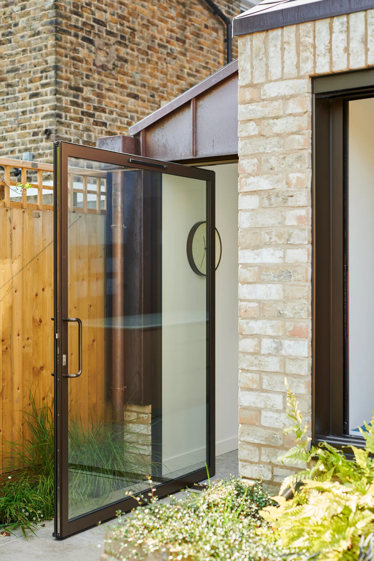 F-Max aluminium pivot door open beside a brick residential entrance