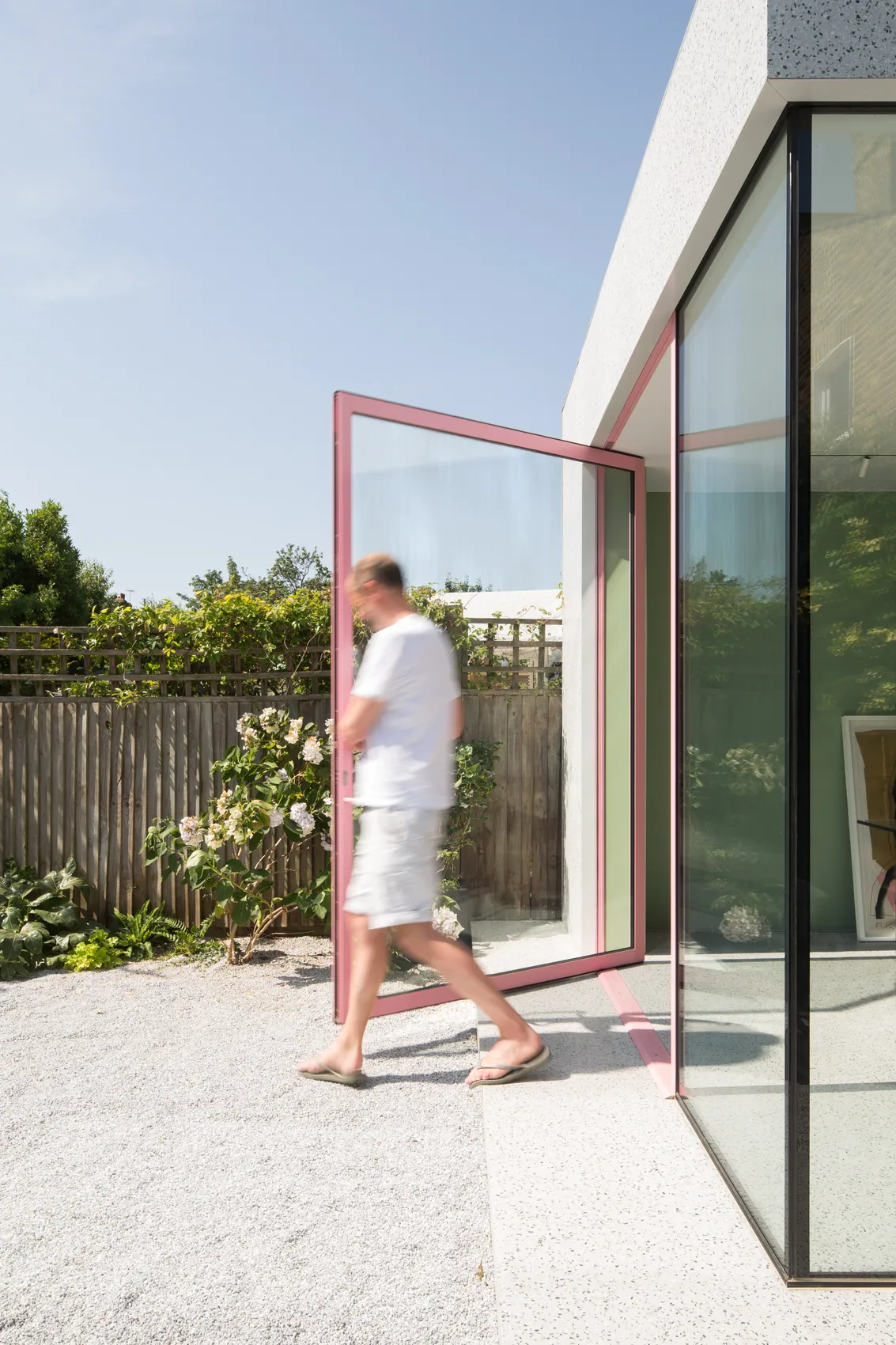 F-Max pivot door open beside a glass corner and garden planting