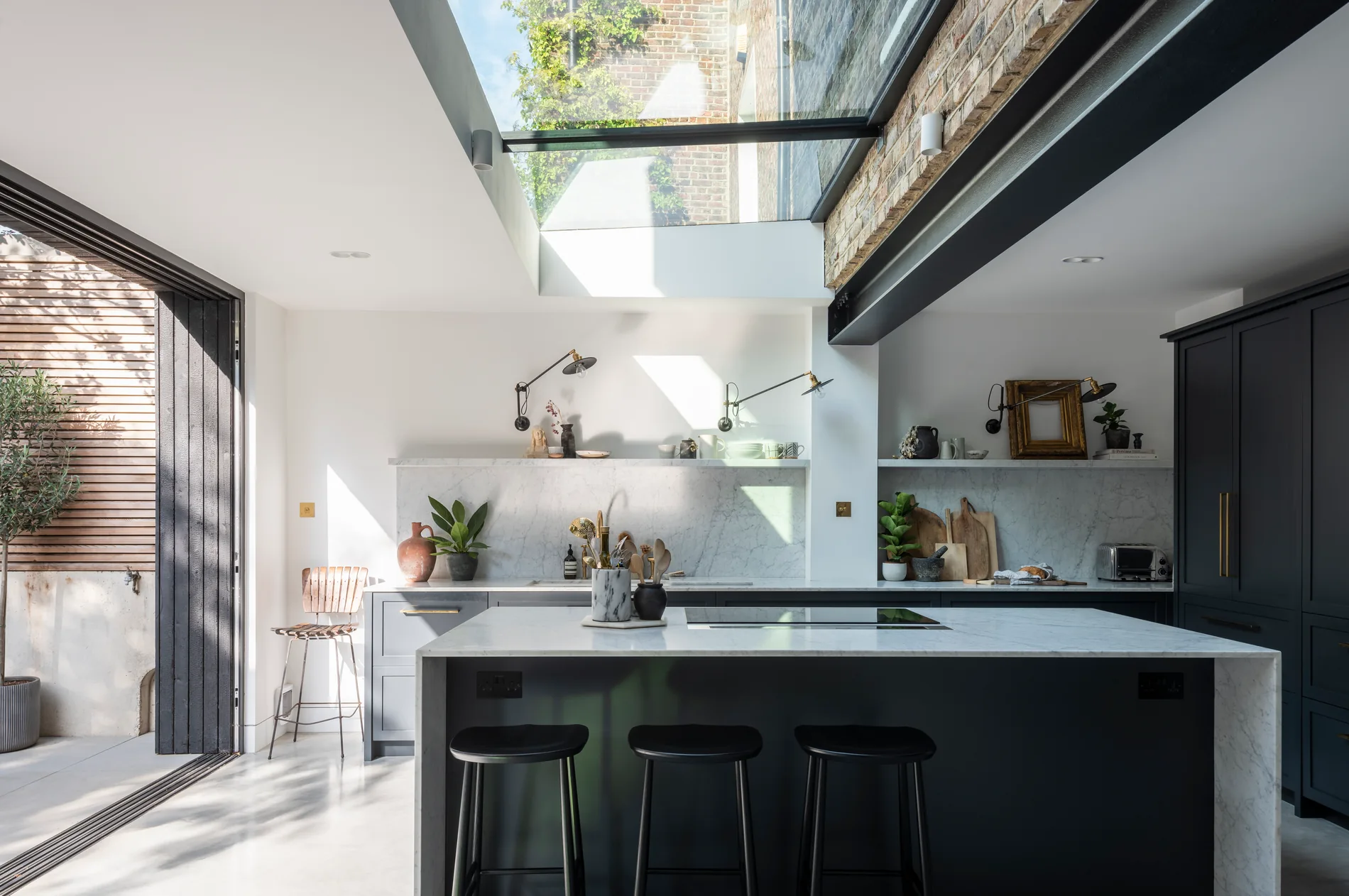 Lean-to rooflight above a contemporary kitchen with dark island, brick wall and steel beam