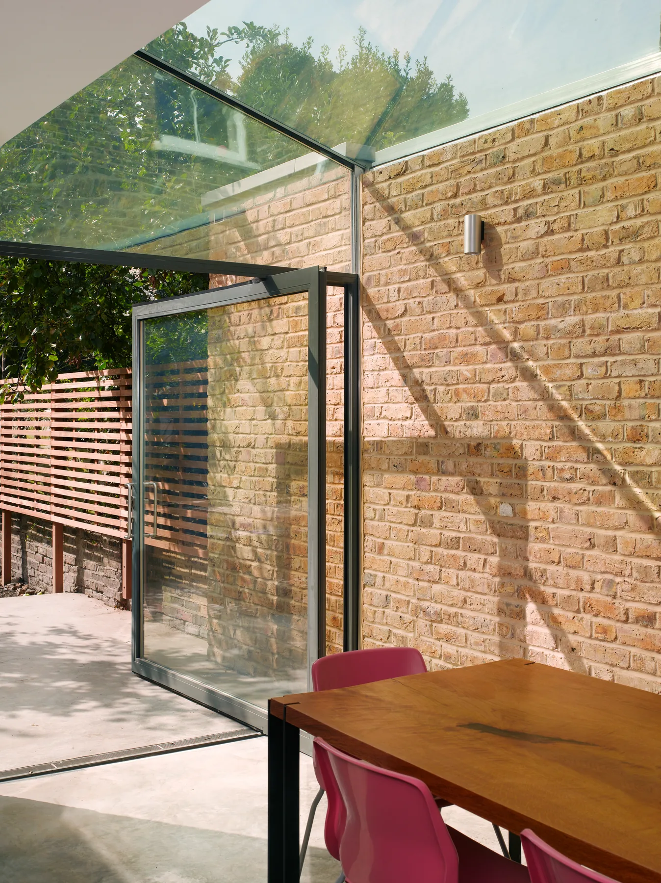 Glazed roof and vertical glass beside a brick wall and red chair
