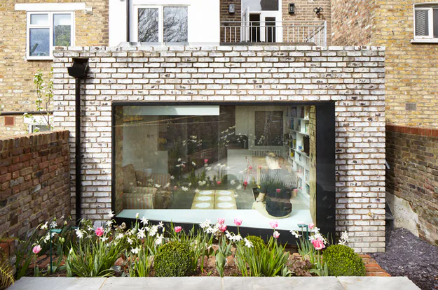 Deep glazed bay opening onto a planted garden from a pale brick extension