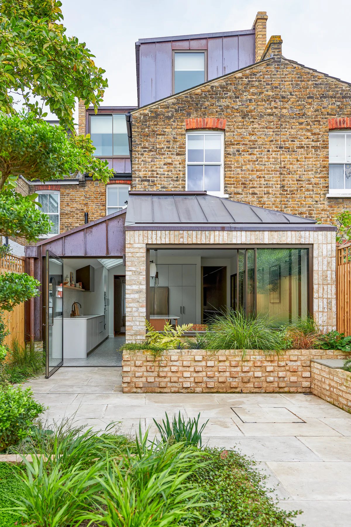 Wide sliding window set into a brick rear extension beside a planted courtyard